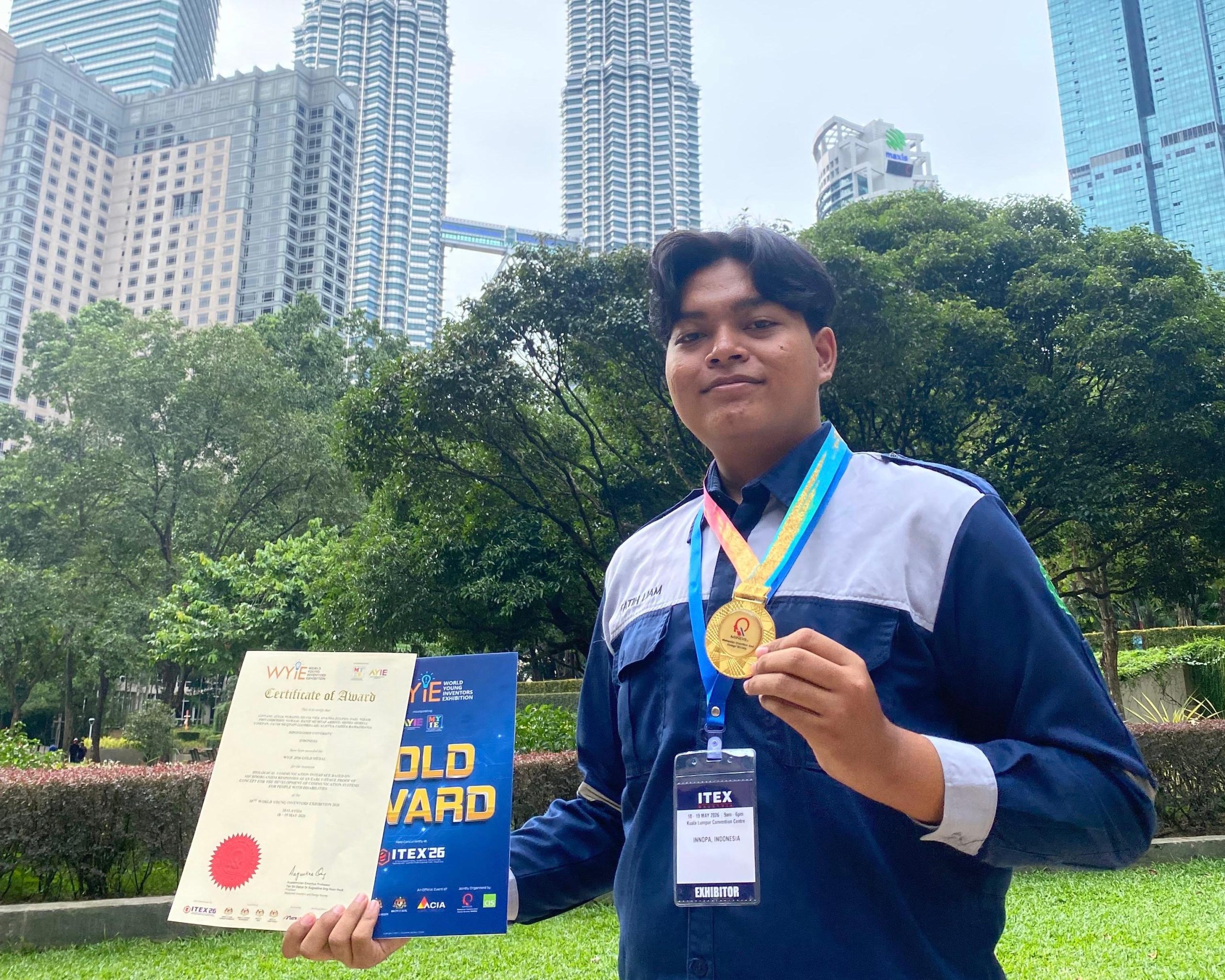 Fatih Muqtafi Liamrillah holding his Gold Award certificate and medal from WYIE 2026 in front of the Petronas Towers, Kuala Lumpur, Malaysia